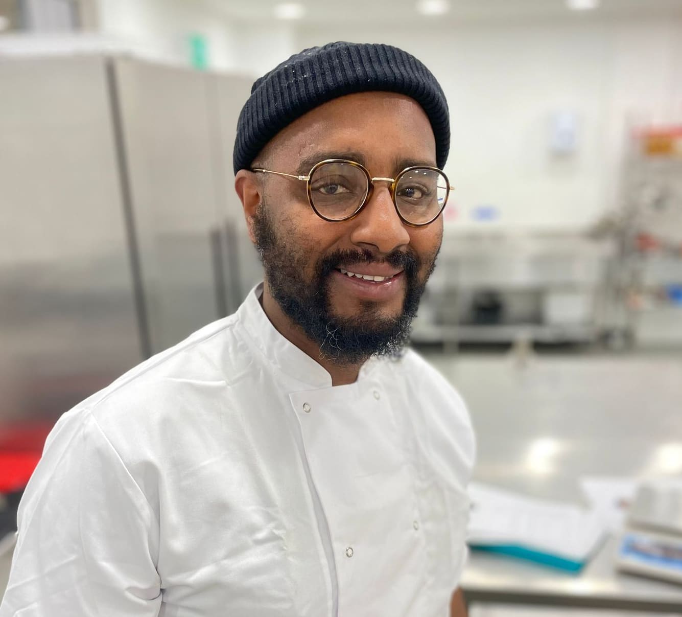 Head of Pastry Quebe with beanie, glasses and chef shirt looking into the camera smiling