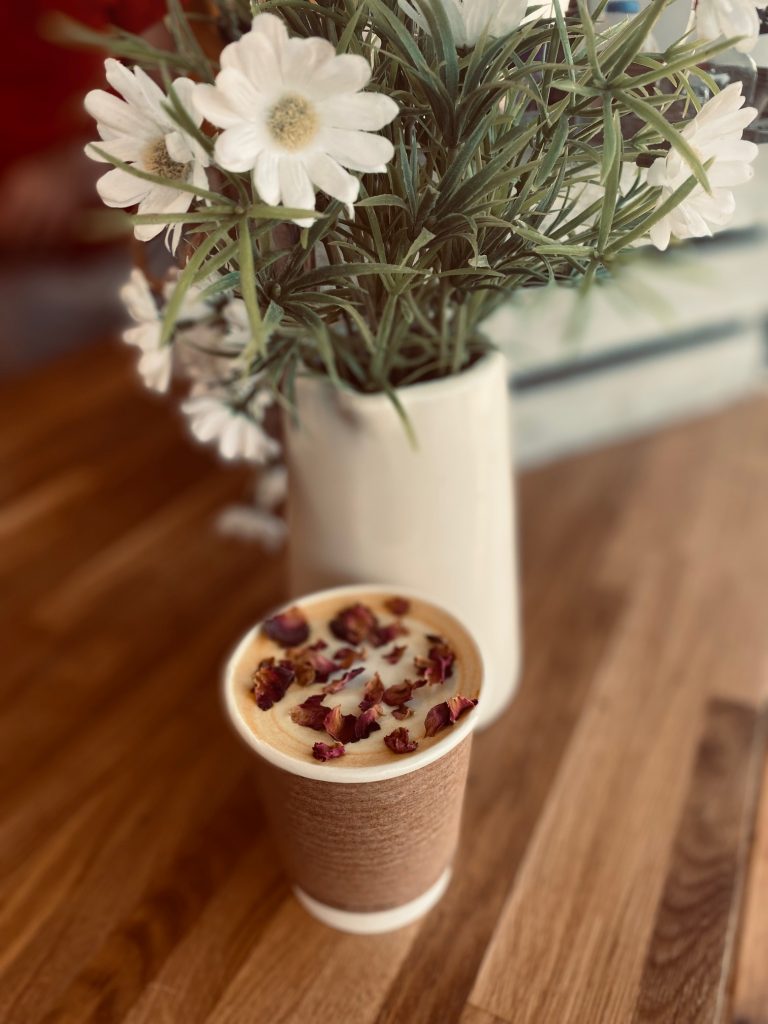 Photograph of a cup of coffee with a vase of flowers in the background.